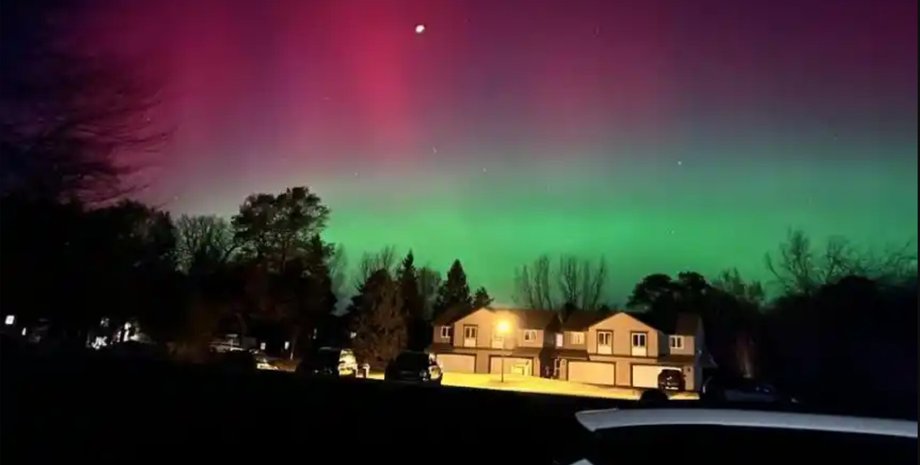 Північне сяйво зелено-рожевих відтінків над будинками і деревами, викликане потужною сонячною бурею