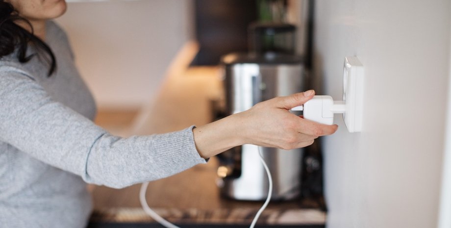 Жінка підключає кавомашину до розетки