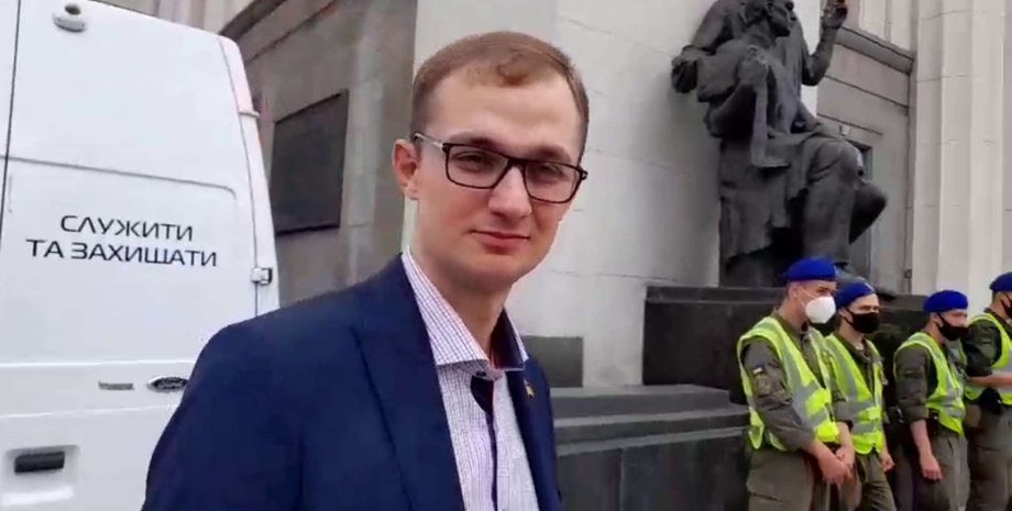 Народный депутат от "Слуги народа" Евгений Брагар на фоне машины с надписью "служить и защищать"