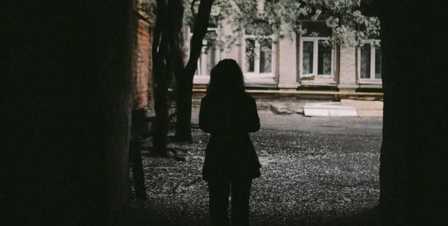 Темний силует дівчини, що стоїть в арці, з видом на подвір'я і будівлю