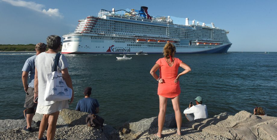 Люди стоять на березі і дивляться на величезний круїзний лайнер Carnival, що йде в море