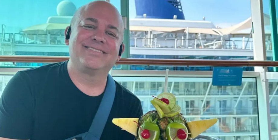 Чоловік зі США посміхається, сидячи на палубі круїзного лайнера з екзотичним напоєм