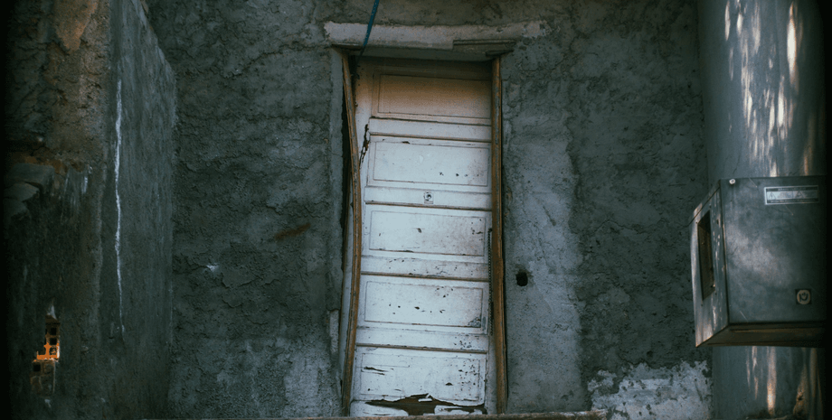 Старі перекошені білі двері в потрісканій бетонній стіні, знайдені господинею під час розчищення саду