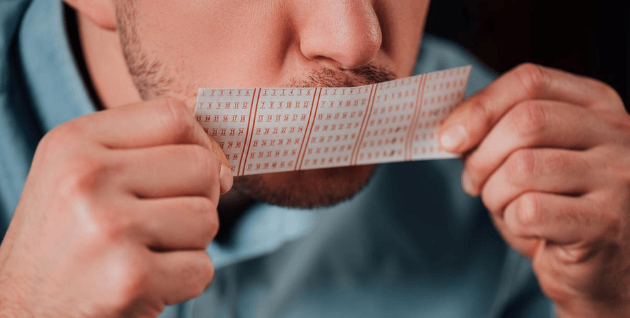Мужчина держит в руках лотерейный билет, который принес ему многомиллионный выигрыш