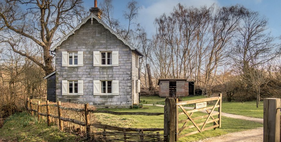 Старовинний будинок із закритими віконницями, оточений парканом і деревами