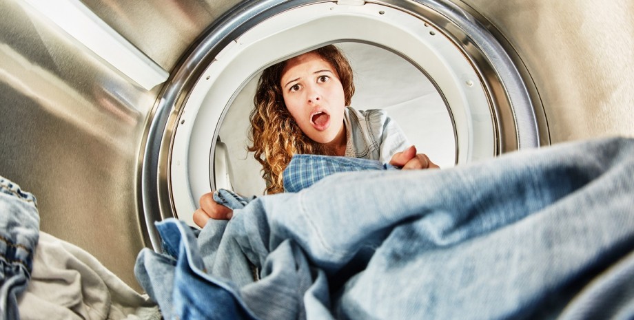Удивленная женщина смотрит в стиральную машину Женщина заглядывает в барабан стиральной машины и с удивлением находит странный предмет среди белья