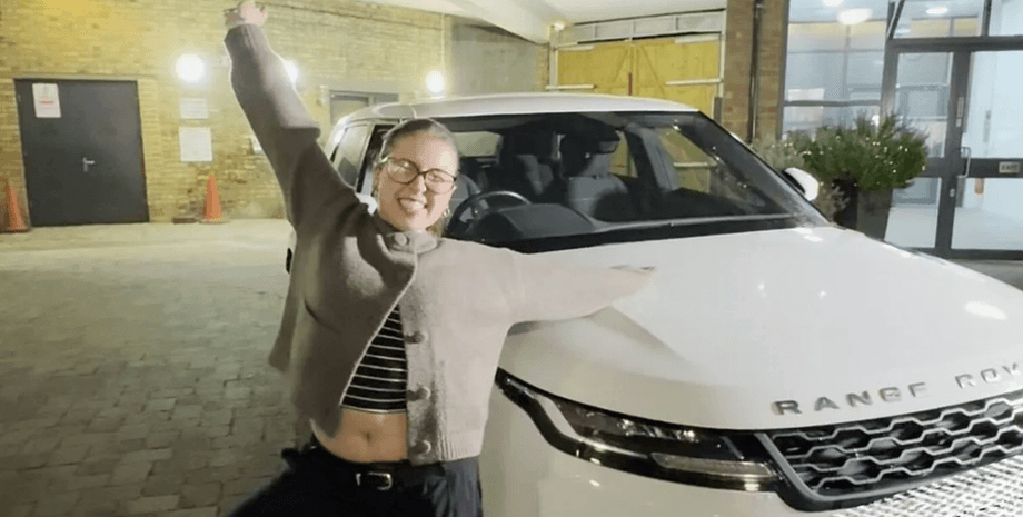 Дівчина позує поруч із білим Range Rover після перемоги в корпоративному різдвяному розіграші