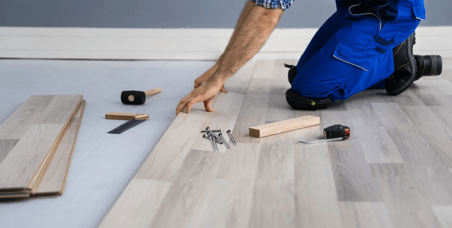 Мужчина укладывает новый ламинат, вокруг лежат инструменты и гвозди