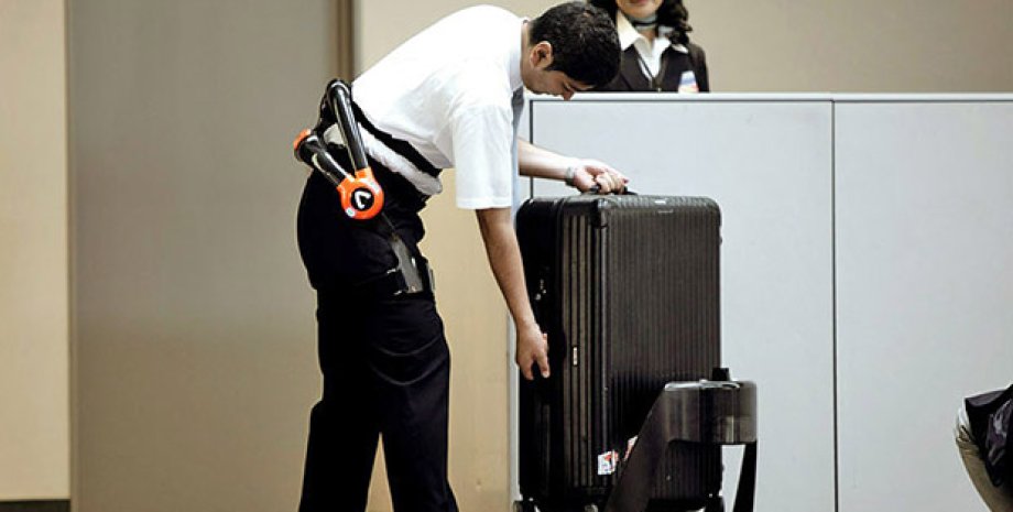 Служащий аэропорта, оснащенный поясом-экзоскелетом грузит багаж на робота-носильщика./ Фото: Japan Airport Terminal Co. / Cyberdyne Inc.