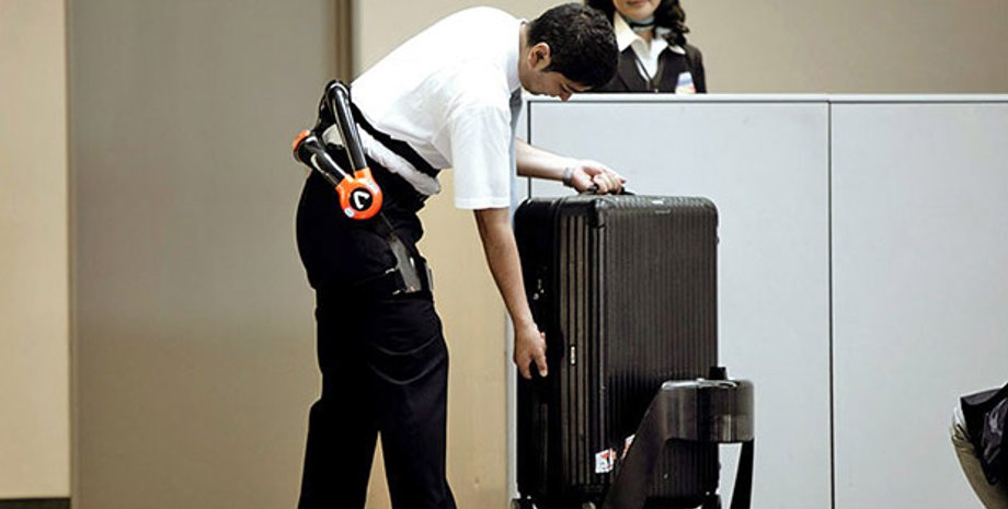 Служащий аэропорта, оснащенный поясом-экзоскелетом грузит багаж на робота-носильщика./ Фото: Japan Airport Terminal Co. / Cyberdyne Inc.