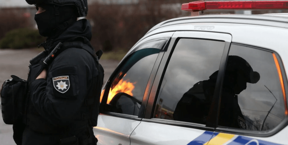 Сотрудник полиции рядом со служебным автомобилем во время работы экстренных служб после взрыва внедорожника