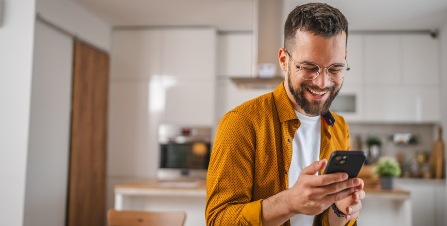 Радостный мужчина со смартфоном в квартире