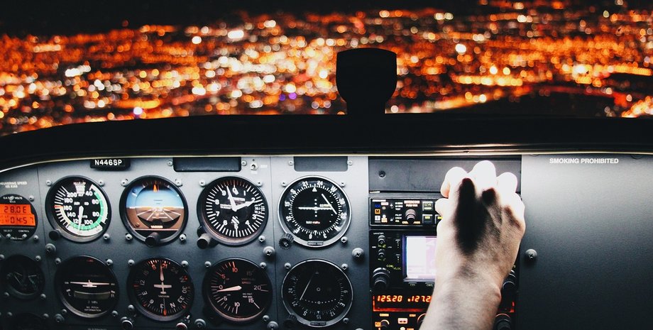 Пилот переключает кнопки в самолете во время полета над огнями большого города