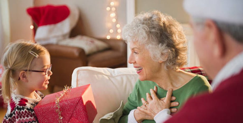 Пожилая бабушка с улыбкой принимает рождественский подарок от внучки