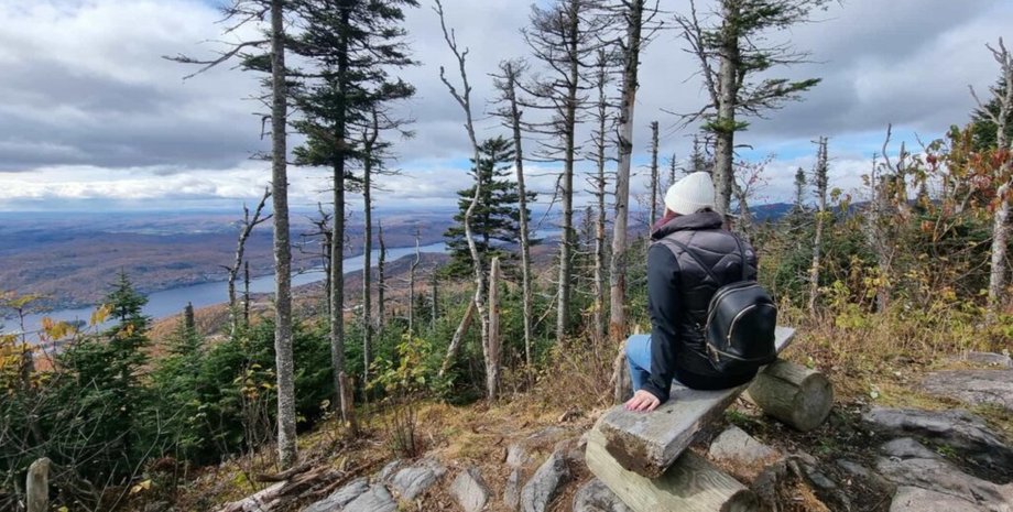 Жінка з рюкзаком сидить на лаві в горах і милується краєвидом на річку та осінній ліс
