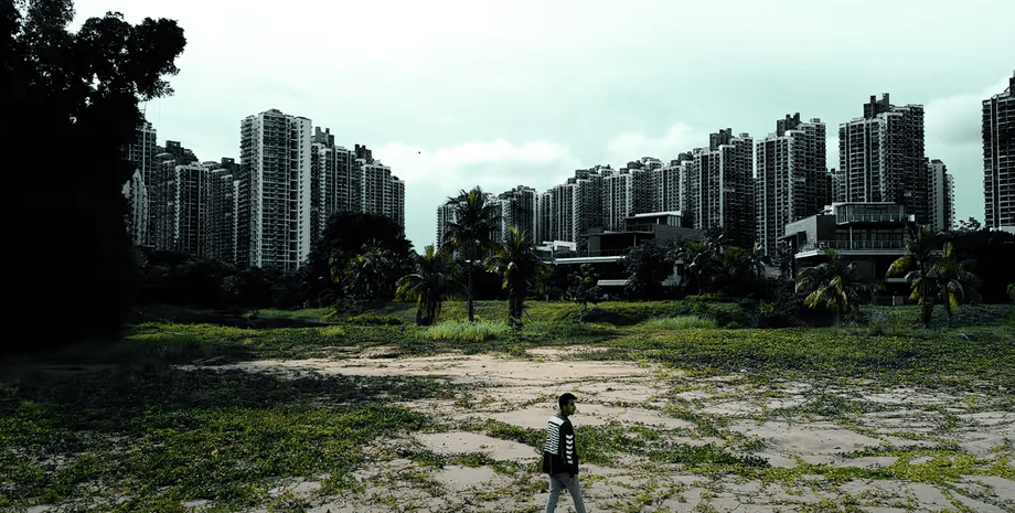 Чоловік іде покинутою територією на тлі величезних, але порожніх житлових комплексів Forest City