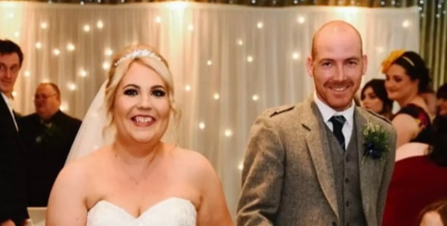 Молодожены улыбаются на свадебном фото, на заднем плане заметен случайный гость