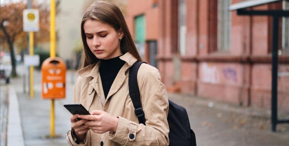 Молодая девушка стоит на улице и смотрит в смартфон