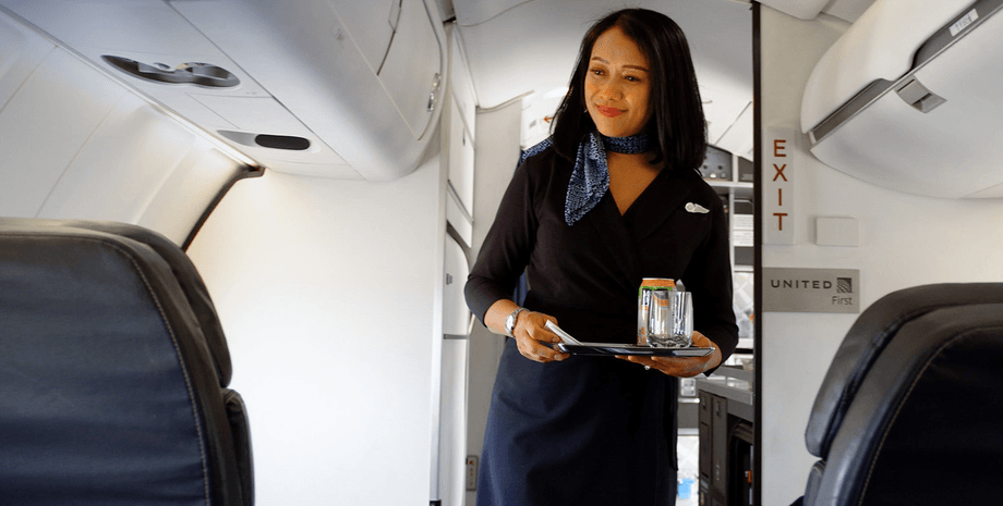Стюардеса з підносом іде салоном літака та обслуговує пасажирів під час польоту
