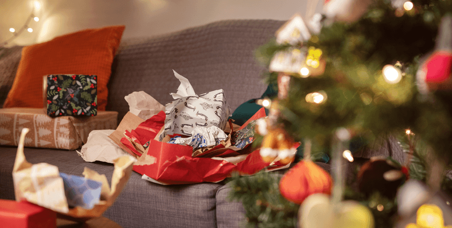 Рождественская оберточная бумага после праздников Разорванная рождественская оберточная бумага и подарочные пакеты на диване после распаковки подарков