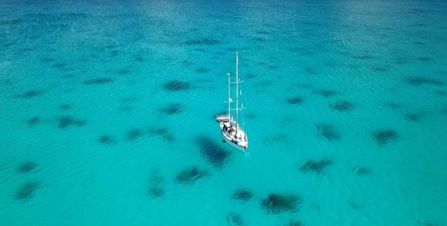 Одинокая яхта на прозрачной голубой воде с темными пятнами рифов