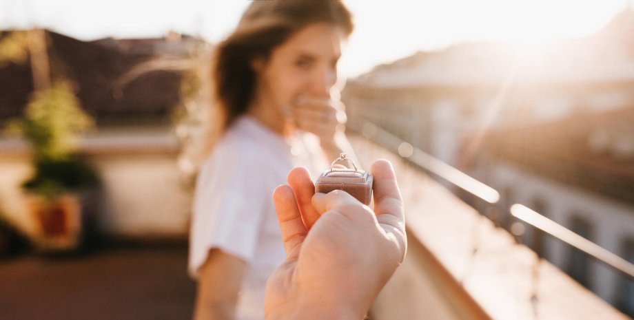 Чоловік простягає коробочку з обручкою жінці під час романтичної пропозиції