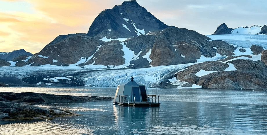 Плавуча хатина в льодовиковій бухті Східної Гренландії на тлі гір і айсбергів на заході сонця