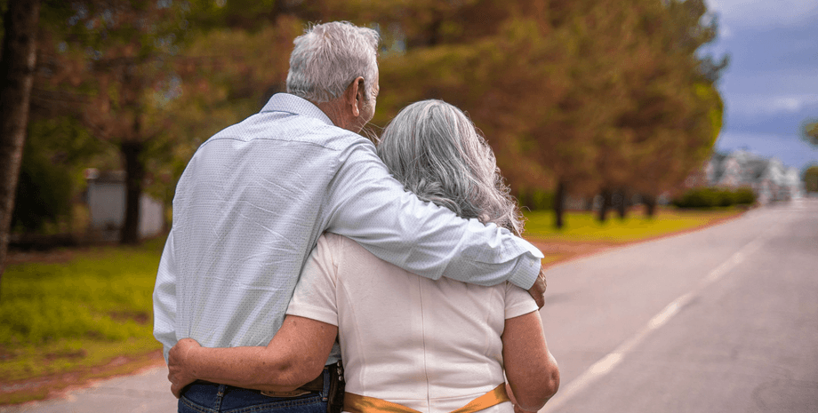 Пожилые супруги идут по дороге, держась за руки