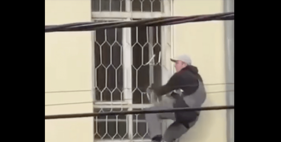 Мужчина спускается по решетке окна