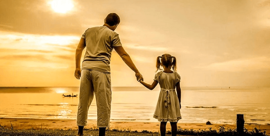 Мужчина держит за руку маленькую девочку на берегу моря на фоне заката