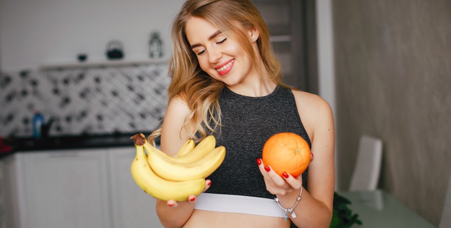 Девушка держит в руках бананы и апельсин