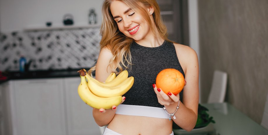 Девушка держит в руках бананы и апельсин
