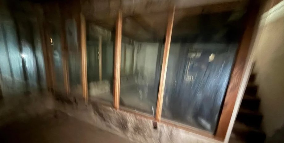 Покинутий підвал з дерев'яними рамами і дзеркальними панелями на стінах, виявлений під люком у вітальні старого будинку