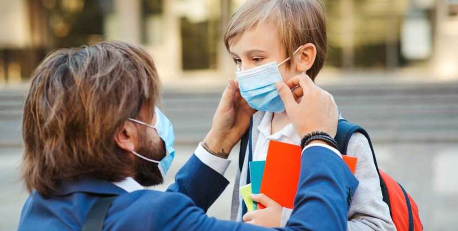 Мужчина надевает сыну-школьнику медицинскую маску из-за эпидемии