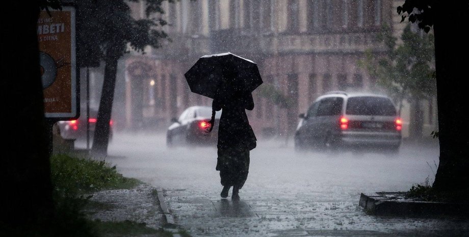 Женщина идет с зонтом под дождем под сильным ливнем в сильный ливень