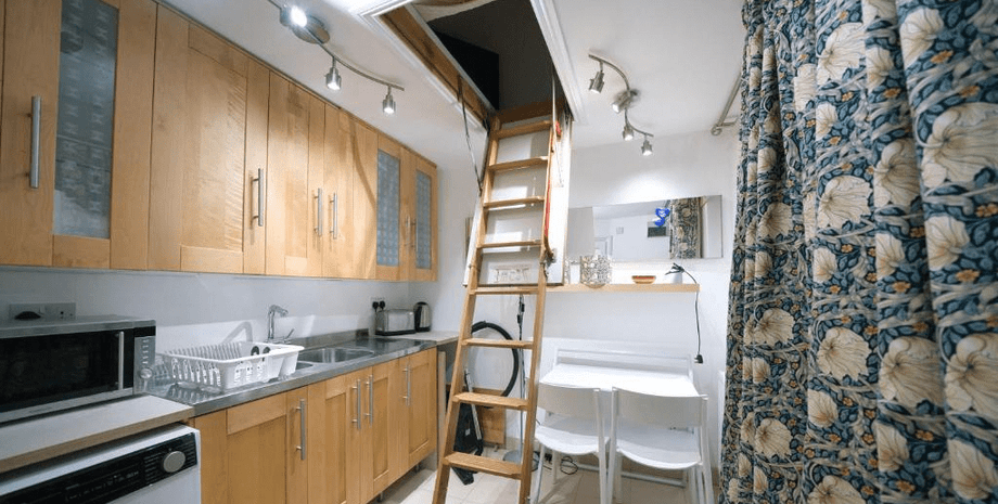 Кухня с деревянными шкафами и лестницей, ведущей в спальню через люк в потолке
