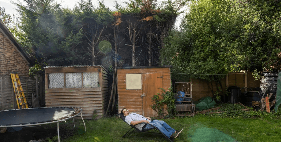 Мужчина лежит в своем саду, затенённом высокой живой изгородью, которая мешает попаданию солнечного света