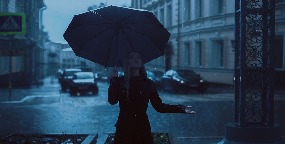 Девушка стоит под дождем в сумерках с зонтом