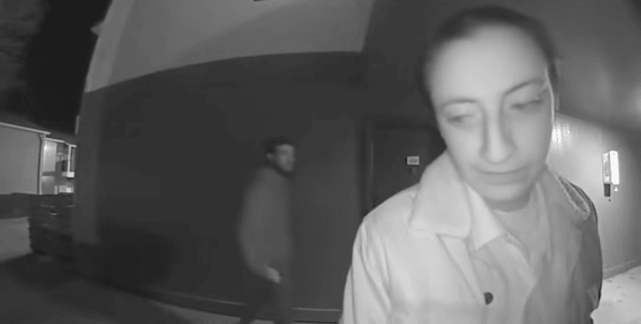 Женщина стоит у двери своей квартиры, а позади нее незаметно приближается неизвестный мужчина