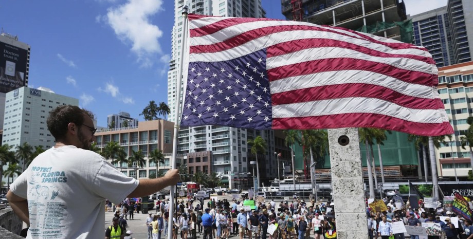 Протестувальник проти політики Трампа тримає перевернутий прапор США 19 квітня 2025 року в Маямі мітинг, сша, американський прапор