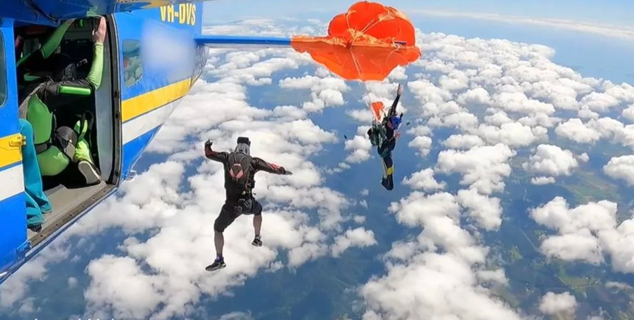 Парашютист отделяется от самолета с распутанным оранжевым запасным парашютом, другие участники прыжка продолжают свободное падение