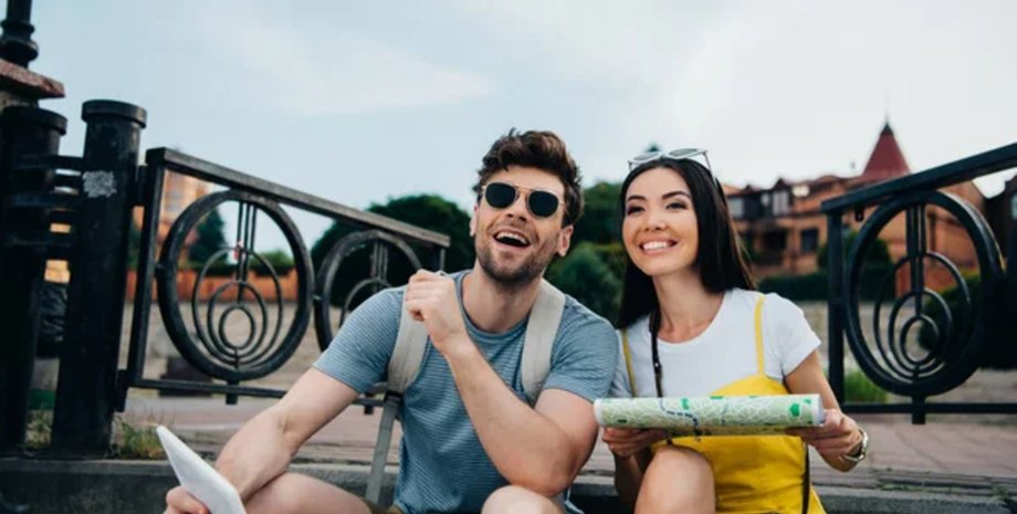 Молодая пара туристов сидит на улице с картой и планшетом, планируя маршрут во время поездки