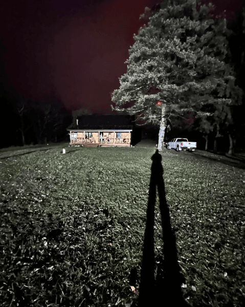 Нічний двір і будинок, залиті яскравим світлом із сусідньої ділянки, через яке територія має вигляд як під прожектором