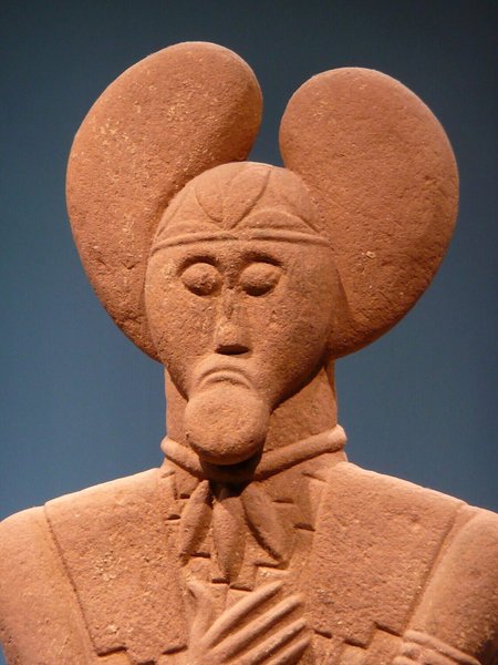 На голові статуї зображено корону з омели