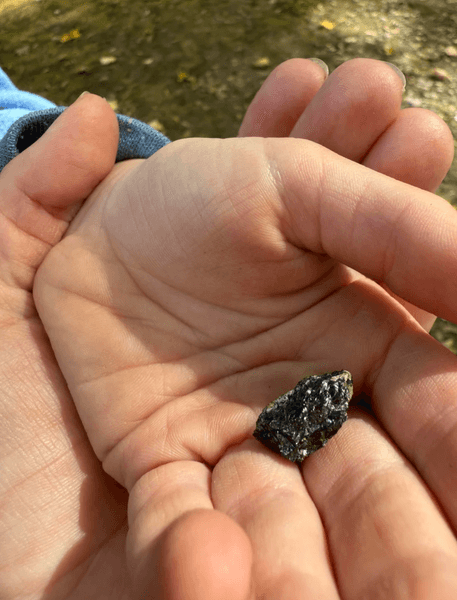 Блискучий чорний камінь у дитячій долоні на тлі землі