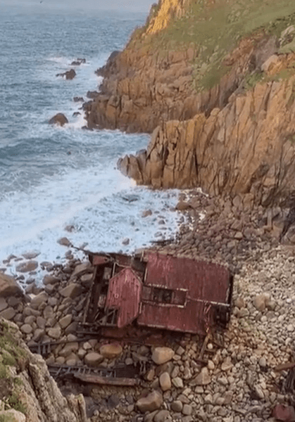 Вид сверху на затонувший корабль в бухте Лендс-Энд у побережья Англии, среди скал и волн