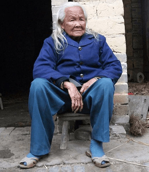 Пожилая женщина Ли Сюфэн сидит у своего дома в китайской деревне