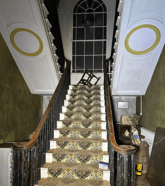 Внутрішні сходи старого будинку з візерунчастим килимом і перекинутим стільцем нагорі