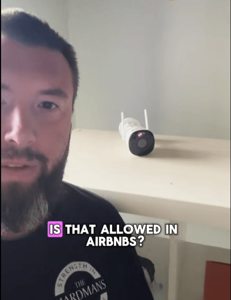 Мужчина снимает себя на фоне включённой камеры наблюдения на полке внутри дома Airbnb