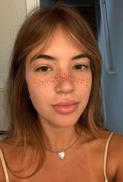 Крупний план обличчя дівчини з нещодавно зробленими татуюваннями у вигляді веснянок на носі та щоках